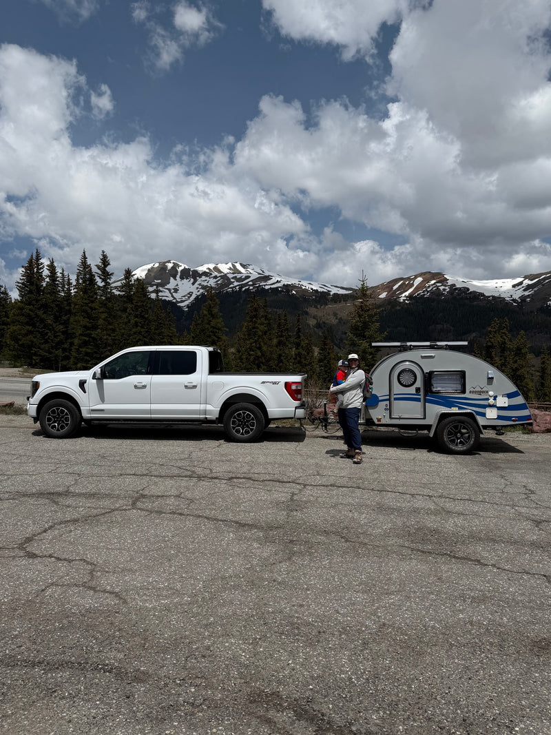 Mountain rv rental trip: White truck, teardrop camper, adult holding child, against snowy peaks & cloudy sky. — photo 6