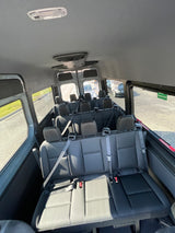 Inside a spacious passenger shuttle van, ideal for RV rental group trips. Features multiple rows of black seats and large windows.