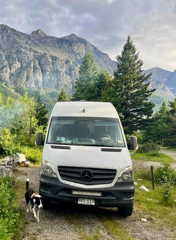 White RV rental van, dog, and majestic mountains. Perfect for scenic van life adventures in a beautiful setting.