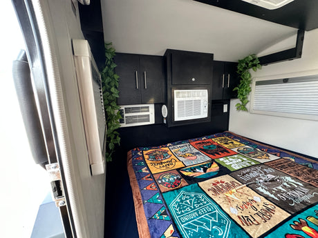 Cozy RV rental bedroom with AC, overhead storage, and a fun camping blanket for adventures.