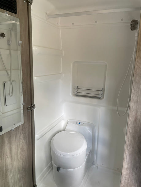 This RV rental's compact bathroom includes an integrated white shower, a modern cassette toilet, and a mirrored cabinet.