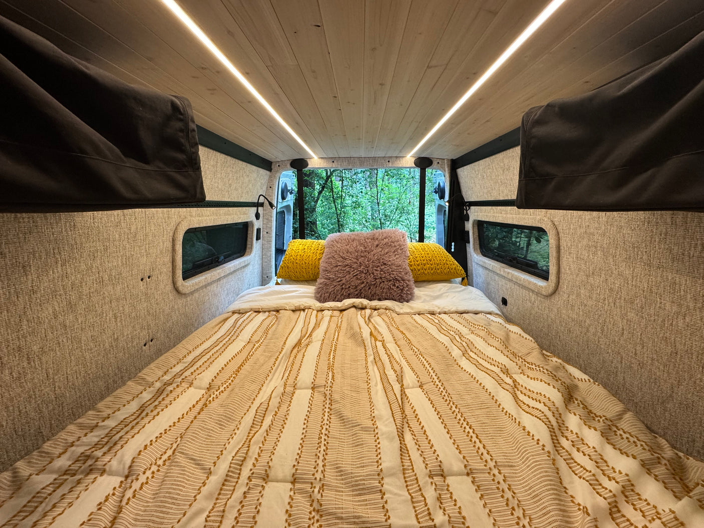 Cozy RV rental interior with bed and forest view from open back doors.