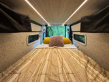 Cozy RV rental interior with bed and forest view from open back doors.
