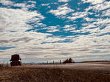 Open road freedom! A dark RV rental van drives on a rural road under an expansive blue sky full of white clouds.