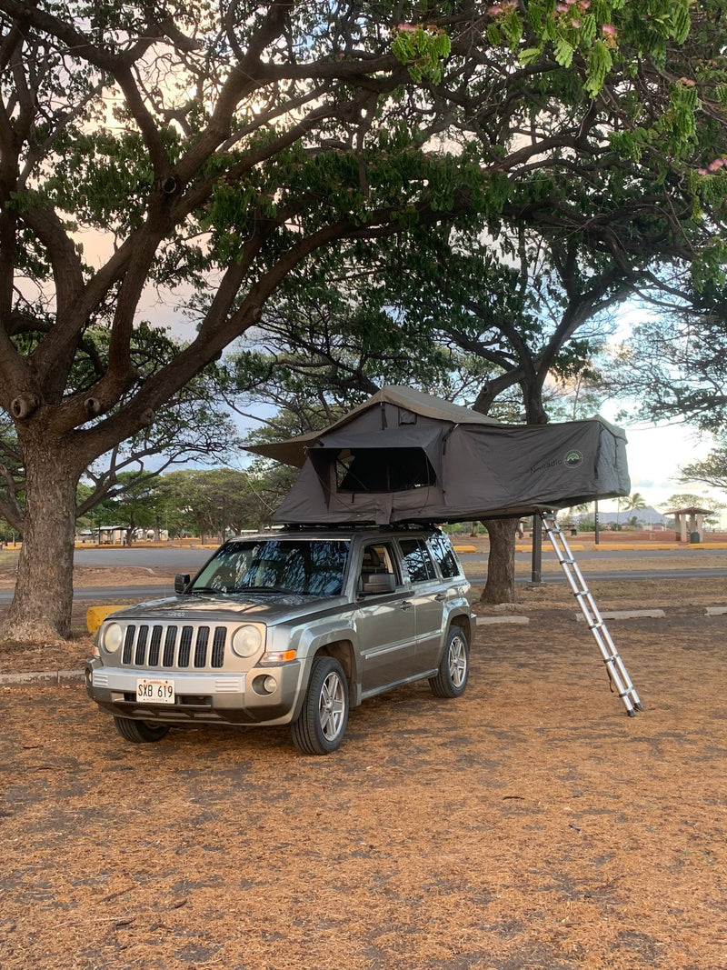 RV rental: A silver Jeep Patriot with an open rooftop tent set up for car camping under lush trees in Hawaii. — photo 14