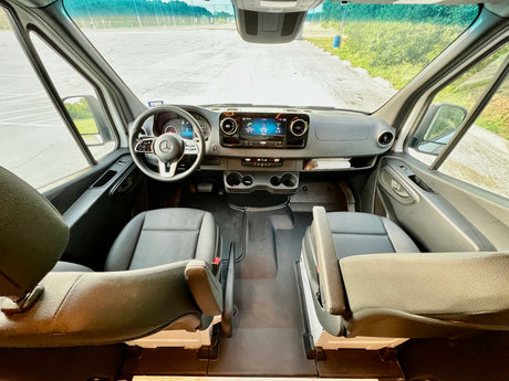 RV rental: The spacious interior of a modern camper van, showcasing the front seats, dashboard, and clear road view.