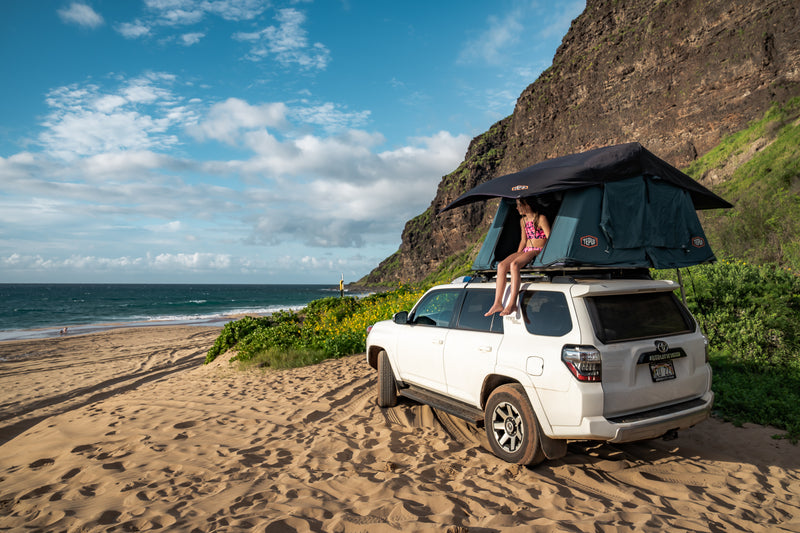 Rooftop tent RV rental on sandy beach in Hawaii. Child sits, overlooking ocean & cliffs. Perfect for outdoor adventure! — photo 1