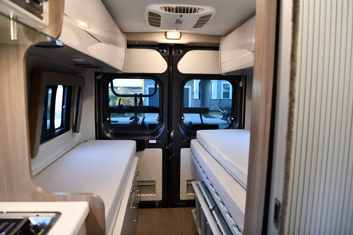 Spacious RV rental interior with convertible sleeping areas on both sides, a kitchen counter, and a view of houses outside.