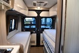 Spacious RV rental interior with convertible sleeping areas on both sides, a kitchen counter, and a view of houses outside.