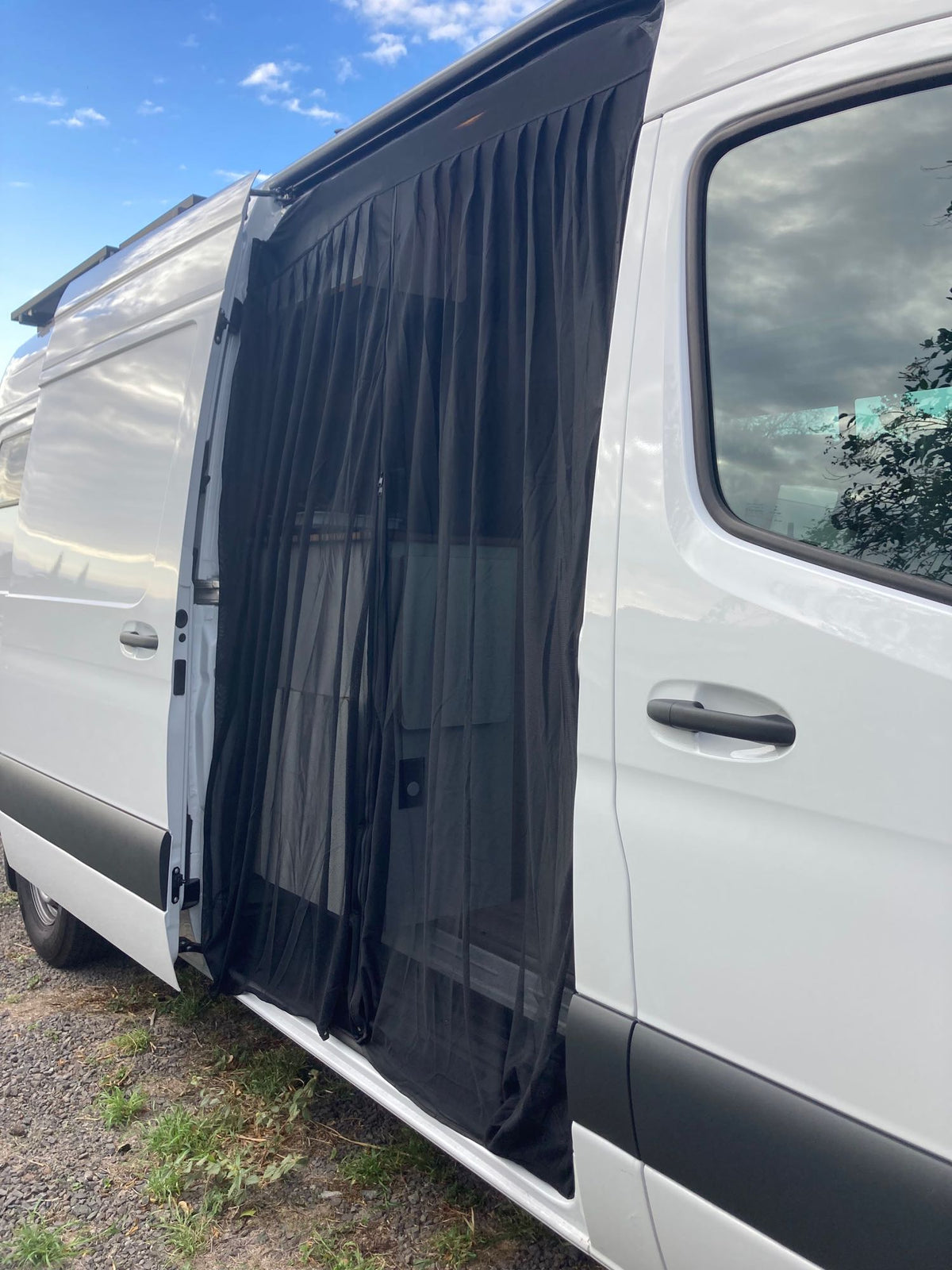  and distant land under cloudy skies.|Scenic RV rental view: a camper van kitchen with stove/sink opens to lush green land and a beautiful ocean vista.|Inside a modern RV rental — photo 19