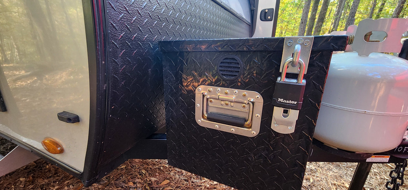 Secure diamond plate storage box with Master Lock & propane tank on RV rental at wooded campsite.