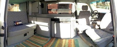 Inside an RV rental: a compact camper van interior with a bench bed, kitchen appliances, and front seats. — photo 11