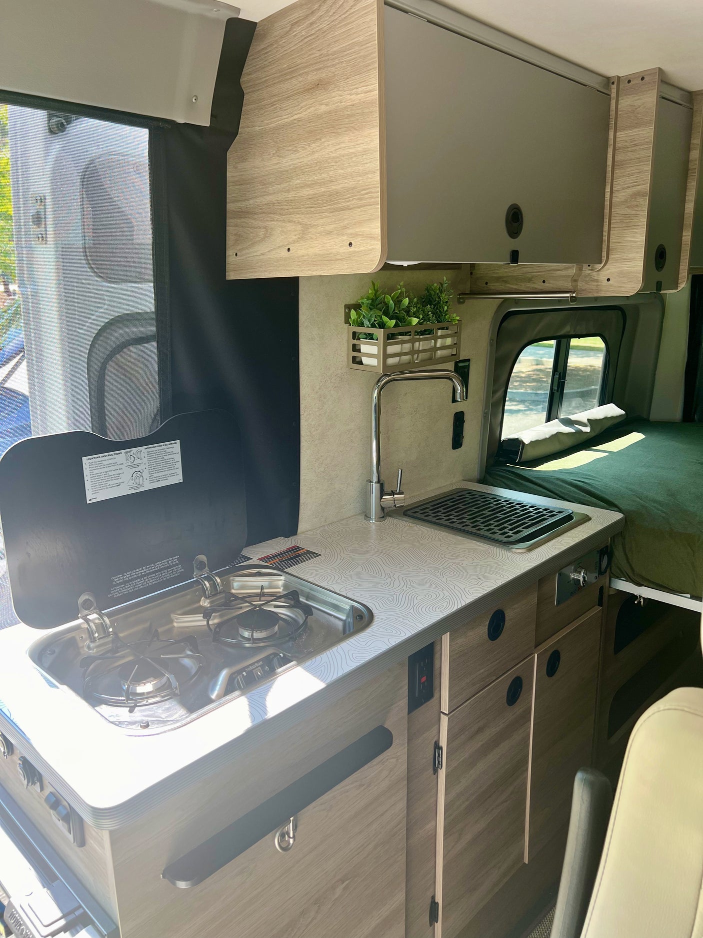 RV rental kitchen: This image shows a compact two-burner stove, sink, patterned countertop, and overhead storage in a camper van.