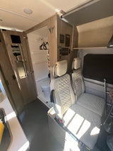 Bright interior of an RV rental, featuring cream quilted seats, a compact wet bath with toilet, and control panels.