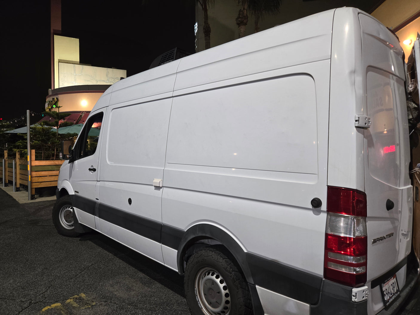 White Mercedes-Benz Sprinter van, likely an RV rental or camper conversion, with a Furrion roof unit, parked at night.