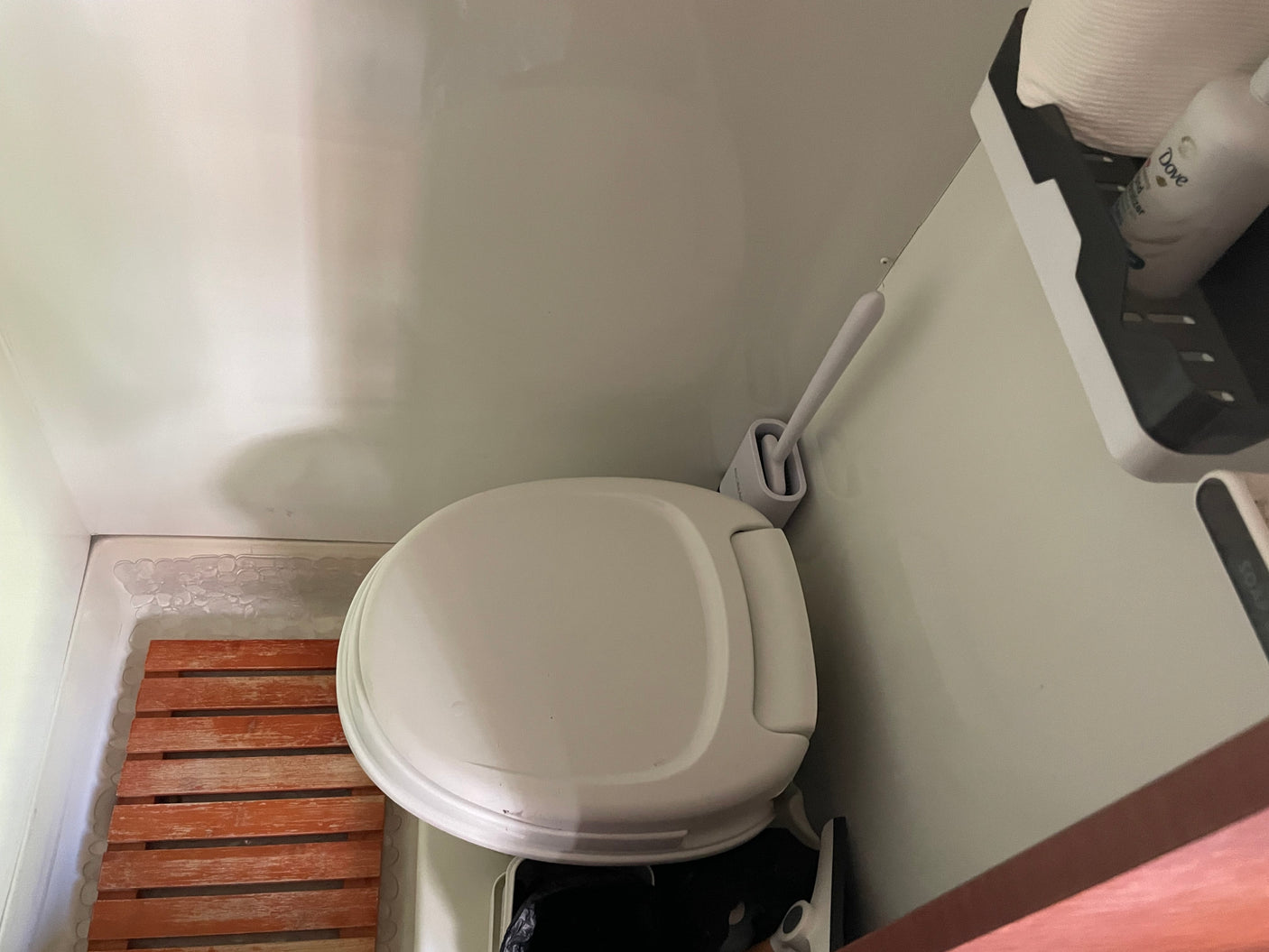 Experience comfort in a compact RV rental bathroom, complete with a clean toilet, wooden mat, and accessible toiletries.