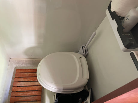 Experience comfort in a compact RV rental bathroom, complete with a clean toilet, wooden mat, and accessible toiletries.