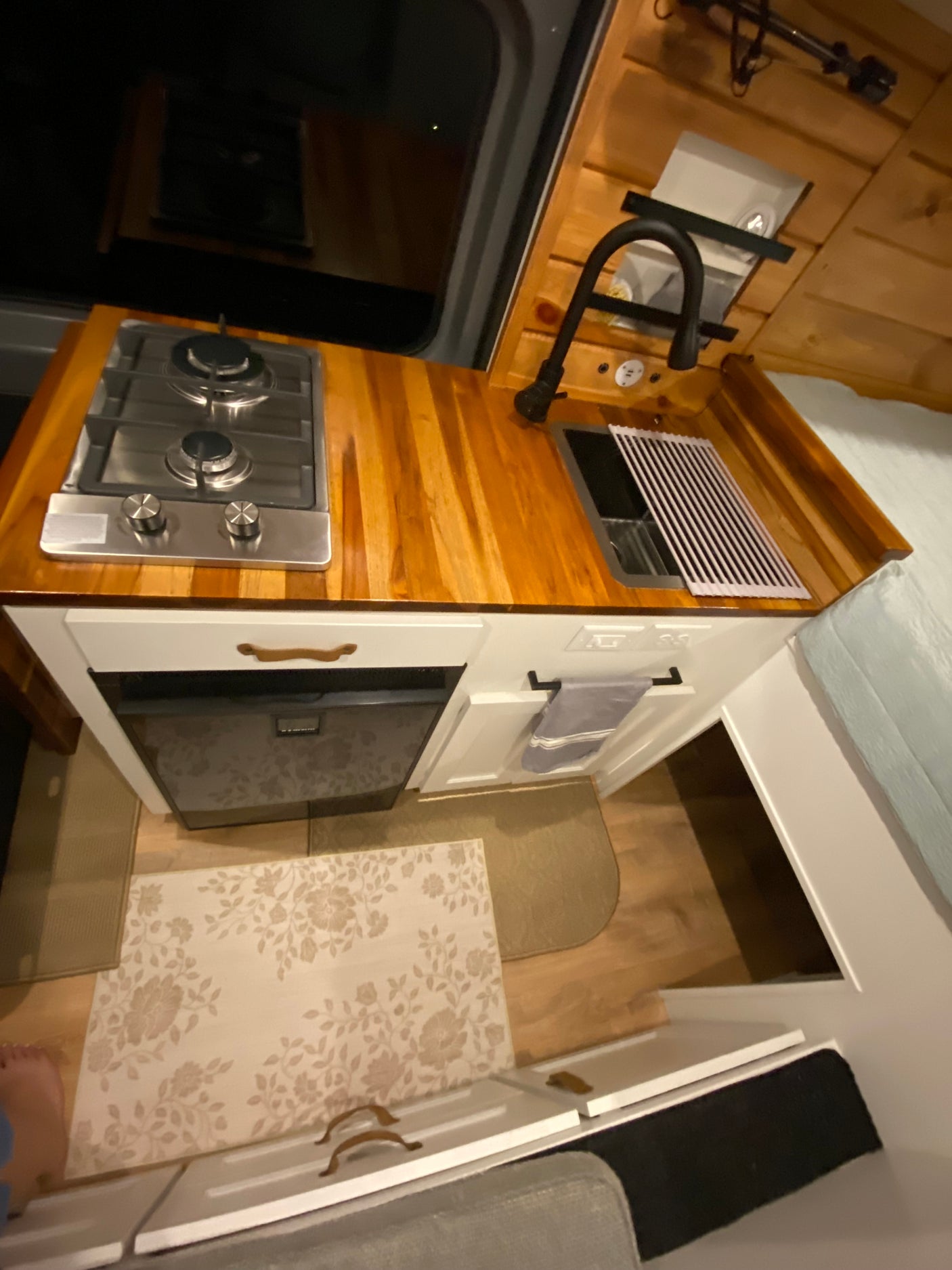 This RV rental features a compact kitchen with a light wood countertop, two-burner stove, black faucet, and built-in fridge.