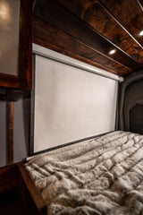 RV rental interior: furry blanket on a comfy bed, with a large pull-down projector screen and dark wood ceiling above.