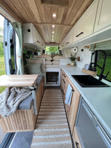 Cozy RV rental interior with custom kitchenette, wood ceiling, comfy bed, and pet kennel visible.