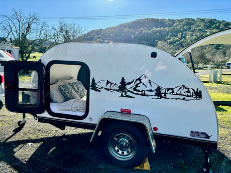 Cozy teardrop RV rental ready for adventure, featuring a scenic mountain decal and open door to its comfy bed.