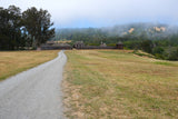 Explore Fort Ross State Historic Park by RV rental. Gravel path leads to the historic wooden fort amidst foggy coastal forests.