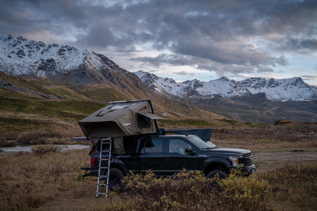 Adventure awaits! Black F-150 with a rooftop tent, a rugged RV rental option, parked in snowy mountains.