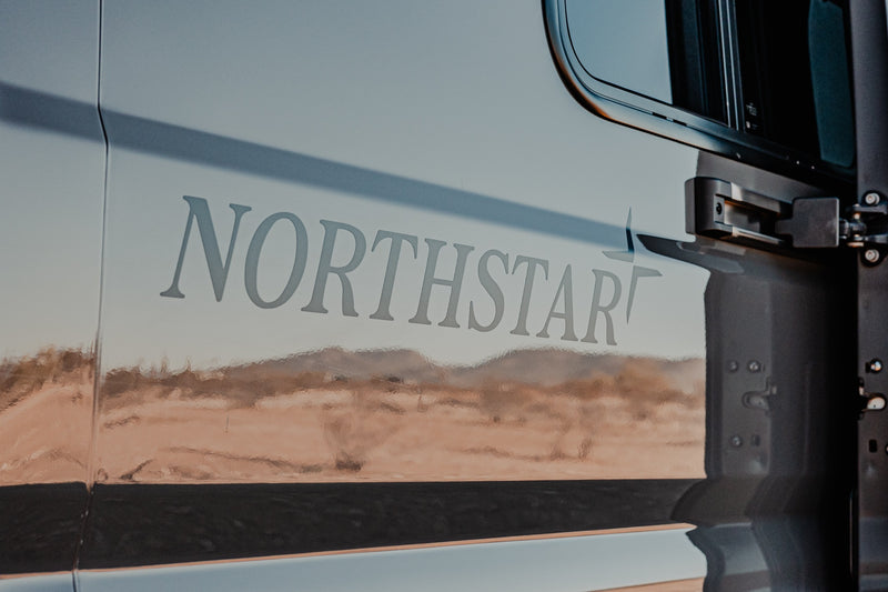 Side of a light gray NORTHSTAR RV rental vehicle, featuring its logo, a window, and warm desert-like reflections. — photo 6