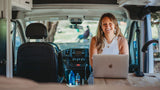 Smiling woman on laptop in RV rental. This mobile office highlights van life and remote work flexibility for travel.