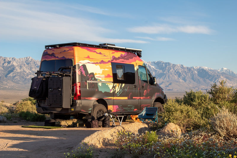 Adventure rv rental van with a vibrant mountain mural parked in a scenic desert campsite with snowy peaks.|Adventure-ready RV rental van with mountain art parked amidst rocks & snow-capped peaks. Perfect for scenic road trips.|Rugged RV rental camper van — photo 1