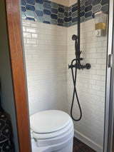 Compact RV rental wet bath with white subway and blue hexagonal tiles, dark shower, toilet, and wood slatted floor.