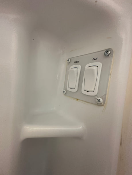 RV rental bathroom: Controls for light and fan in a compact, white shower stall with an integrated shelf, commonly found in RVs.