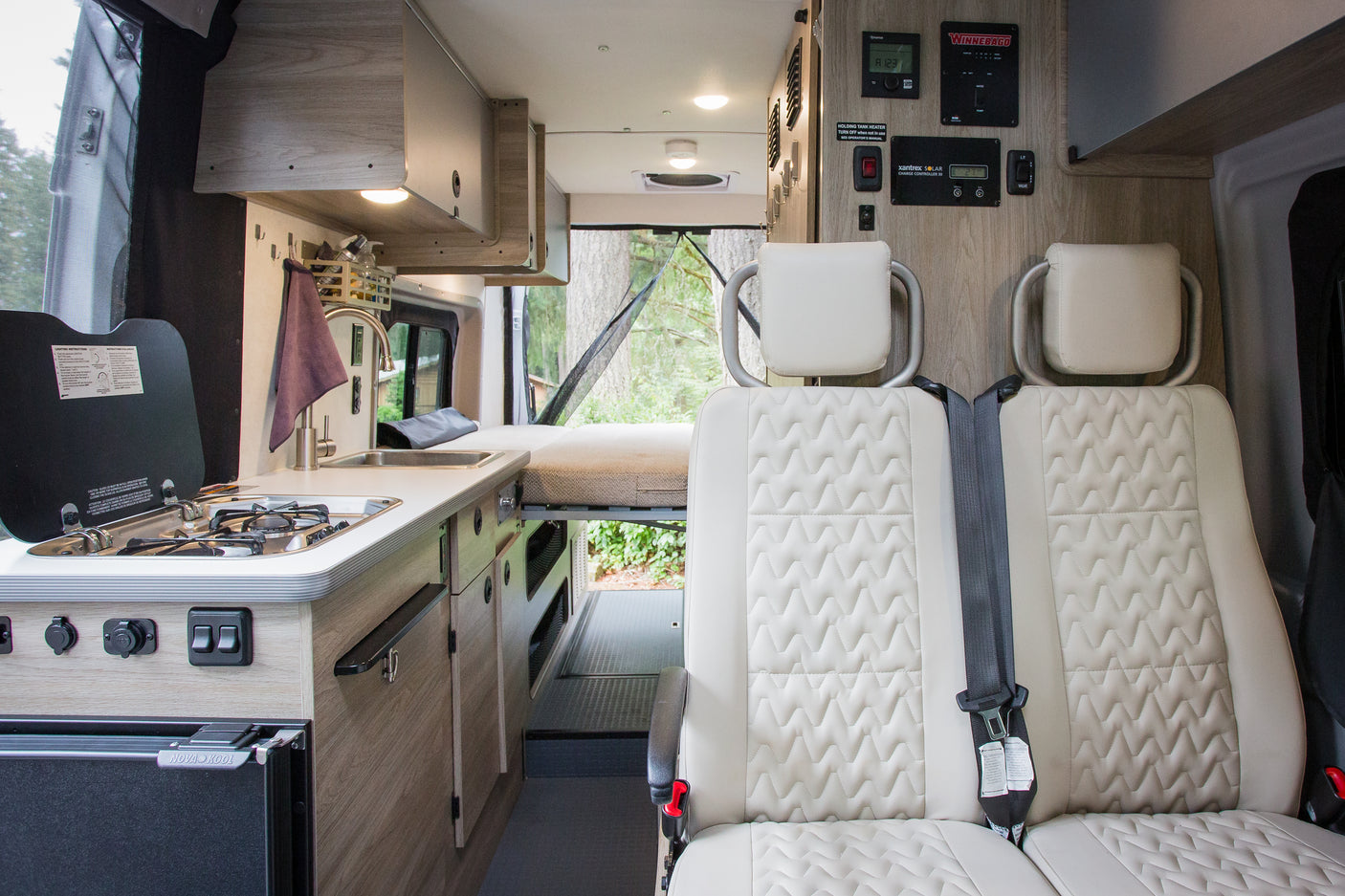 RV rental interior: light wood cabinets, quilted seats, kitchen, rear bed, and tech controls for a comfortable journey.