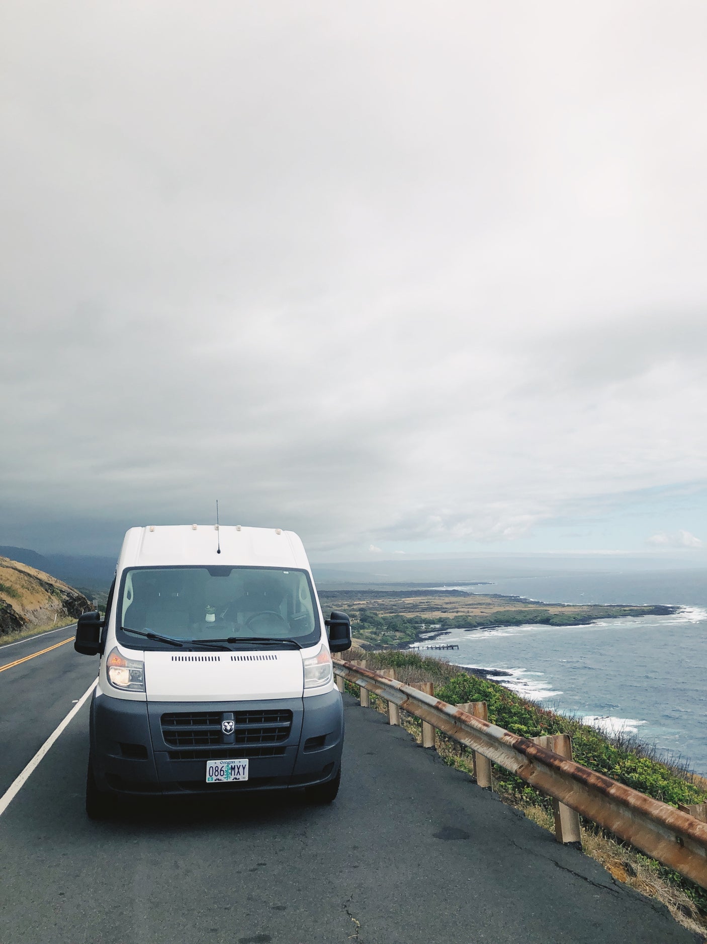 White RV rental van on a scenic coastal road. Ocean views and cloudy skies make for a picturesque road trip adventure.
