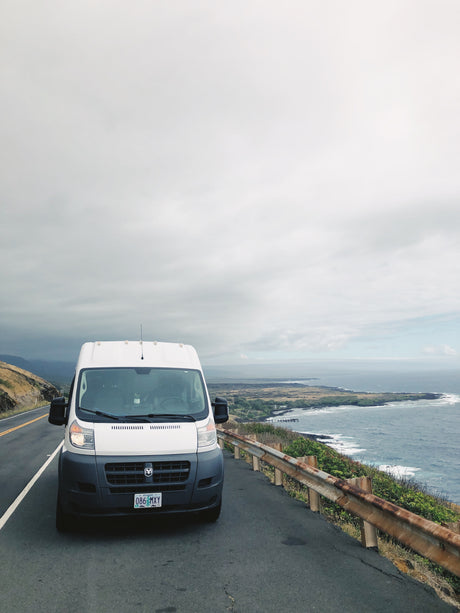White RV rental van on a scenic coastal road. Ocean views and cloudy skies make for a picturesque road trip adventure.