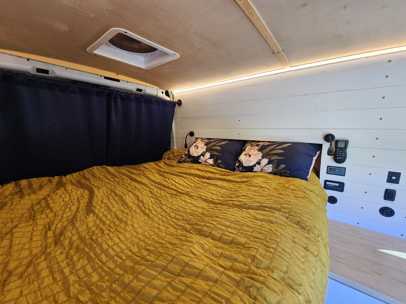 Inside a comfortable RV rental: A bed with a yellow comforter, floral pillows, and wall-mounted controls. — photo 11
