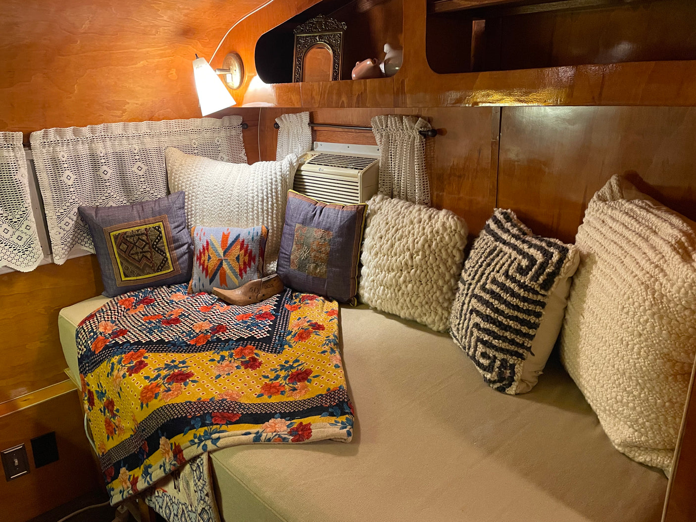 Experience a comfortable RV rental interior: soft pillows, a colorful blanket, and an AC unit for a cozy stay.