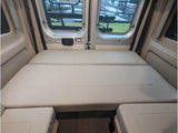 Inside an RV rental camper van: A large, light-colored, multi-section bed fills the rear, offering ample sleeping space.