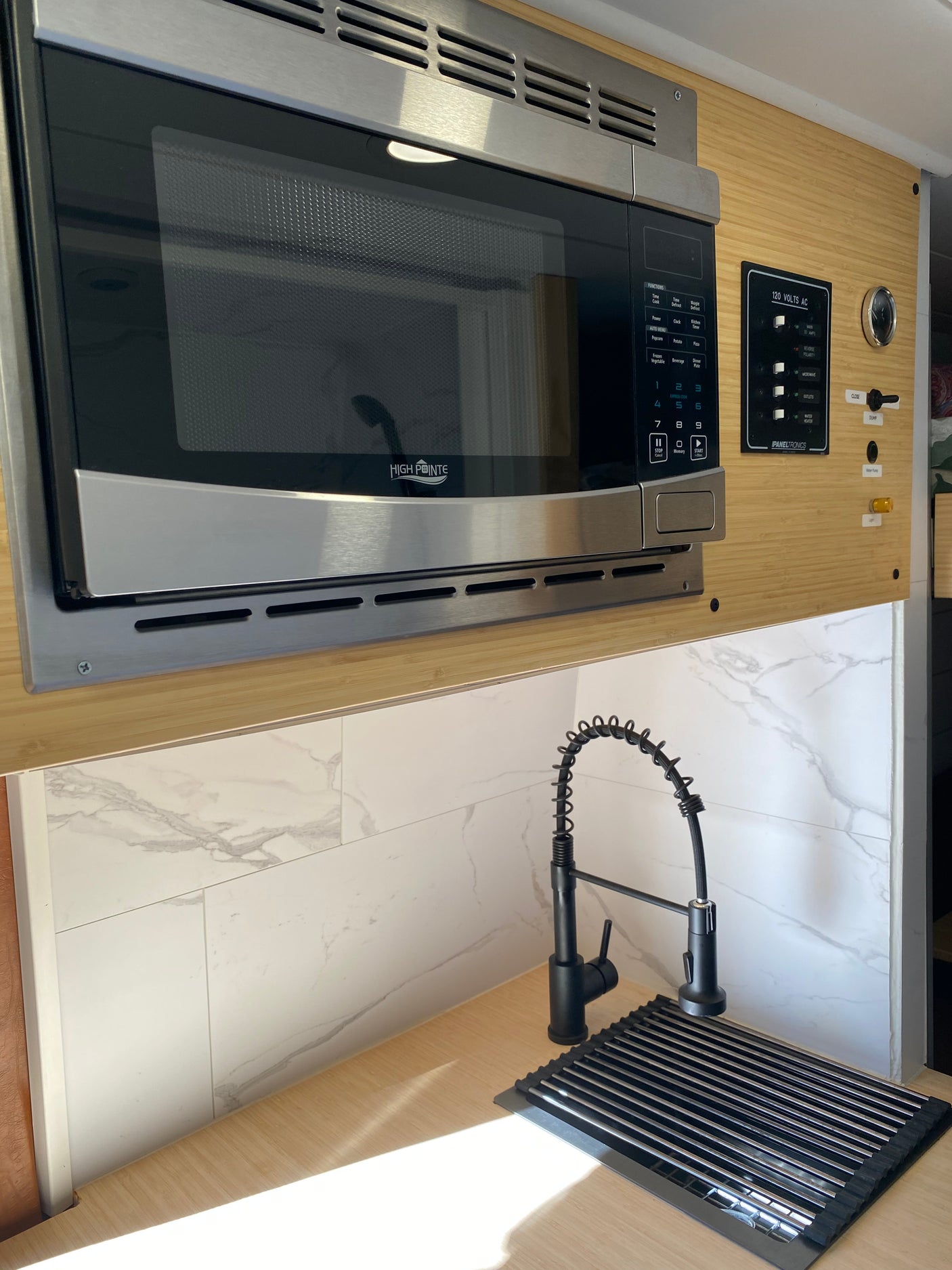 Modern RV rental kitchen featuring a High Pointe microwave, black pre-rinse faucet, and Paneltronics control panel.