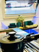 Inside an RV rental: A cooking pot on the stove. Teal dishes, a plant, & a window are visible in the bright kitchen space.