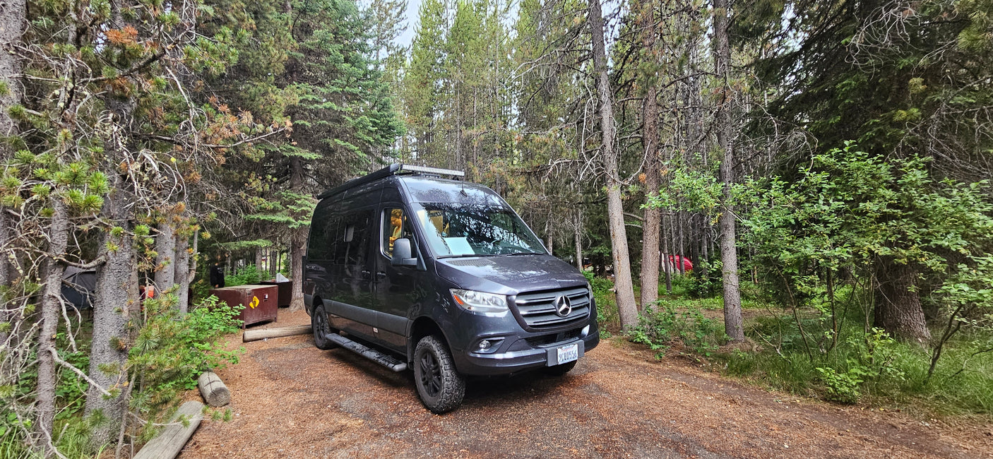 Experience van life! This rv rental is parked at a shaded forest campsite, perfect for outdoor adventures.