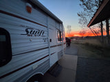 Stunning sunset over an RV rental: a Jayco travel trailer parked in nature with a vivid orange and red sky.