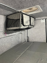 RV rental interior featuring practical overhead storage, a roof vent fan, and modular grey bed cushions for comfortable travel.