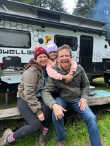 A happy family poses with their modern RV rental, a white travel trailer perfect for camping trips.