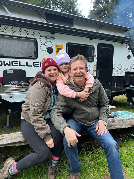 A happy family poses with their modern RV rental, a white travel trailer perfect for camping trips.