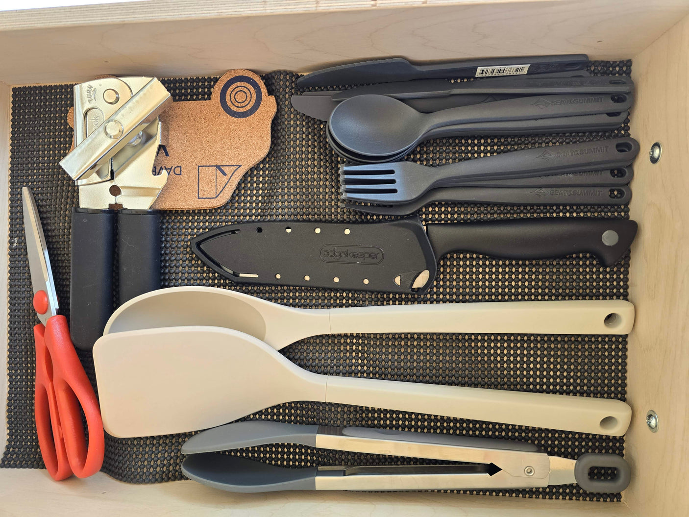 RV rental kitchen drawer with camping gear: Sea to Summit cutlery, cooking tools, knife, can opener on non-slip mat.