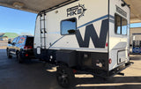 A Winnebago Hike RV rental, an off-road travel trailer, towed by an SUV, parked at a gas station, ready for adventure.