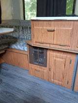 RV rental interior: cozy dinette with patterned cushions, wood-grain cabinets, and kitchen stove.