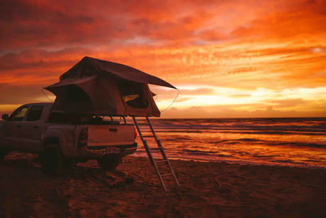 Experience beach camping with an RV rental! Truck with rooftop tent at sunset by the ocean.