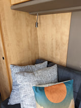 Cozy RV rental interior with light wood paneling, a reading light, and comfortable pillows on a dark grey sofa.